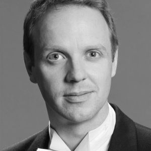 A man with short hair wearing a white shirt and black jacket.