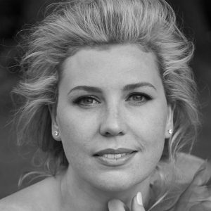 A woman with blonde hair with her hand to her neck.