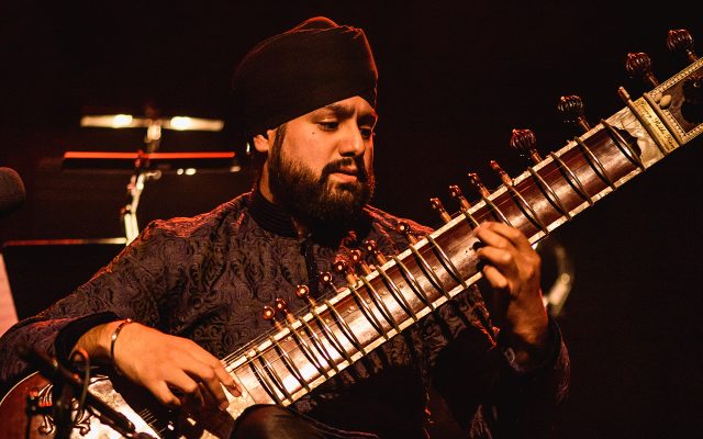 A young Sikh musician plays the sitar on a darkened stage