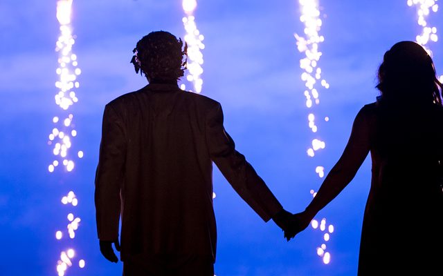 The silhouette of two people holding hands as sparks fall from above.