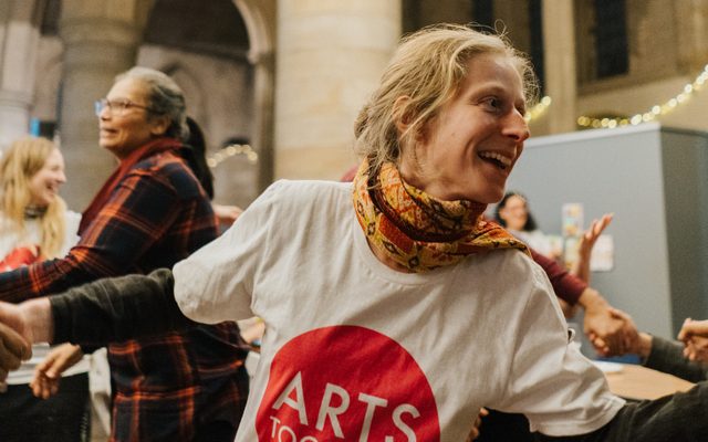 Girl in Arts Together t-shirt laughing and holding hands with other people at celebration