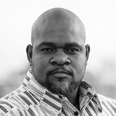 A bearded man wearing a striped shirt, looking into the camera