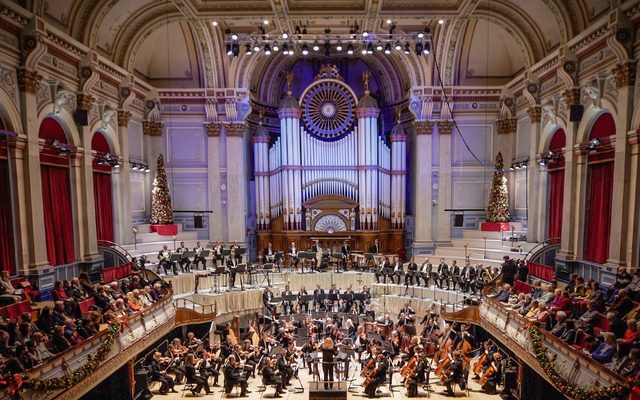 A large orchestra on stage in an ornate Victorian town hall