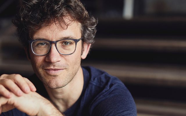 A man wearing glasses and smiling sitting on a staircase