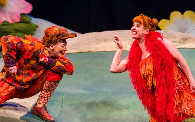 Two people dressed as foxes crouched on the flower laughing together.