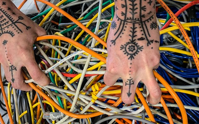 A hand covered in tattoos grasping a lot of cables.