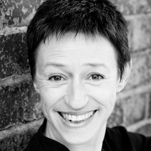 A woman with short hair stood in front of a brick wall.