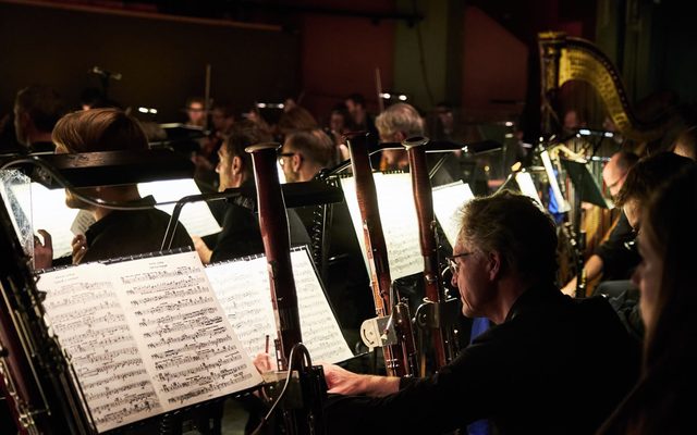 Musicians play bassoons in a dark space with light on their sheet music.