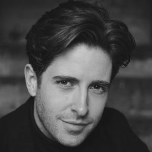 A man with short dark hair wearing a dark suit.