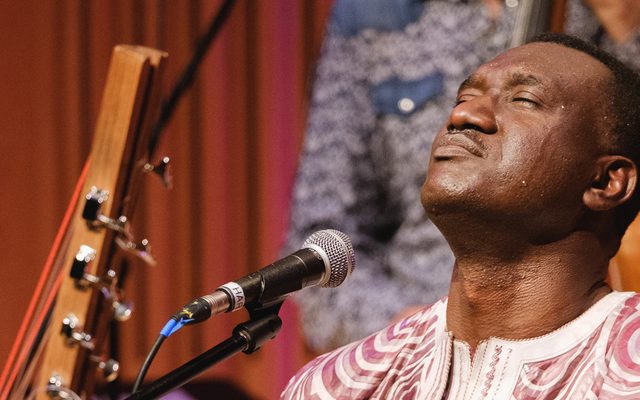 Closeup of a male musicians' head, tilted back with eyes closed, and beads of perspiration on his face