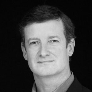 A man with short dark hair wearing a shirt and jacket.