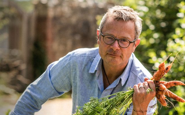 A man in a blue shirt clutching some carrots.