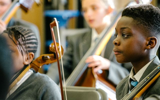 A young member of Opera North's In Harmony education programme holding a violin at a rehearsal