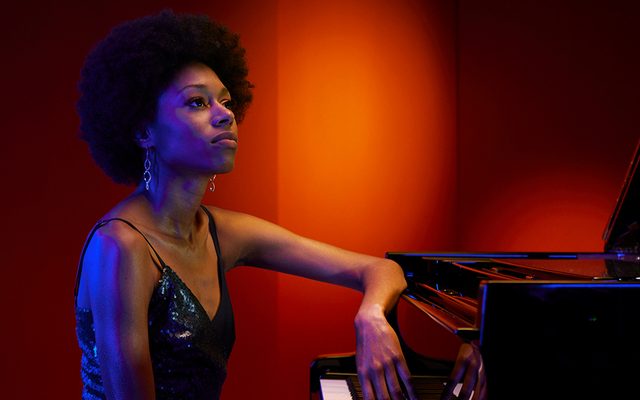 A woman sat at a piano leaning on it with one hand.