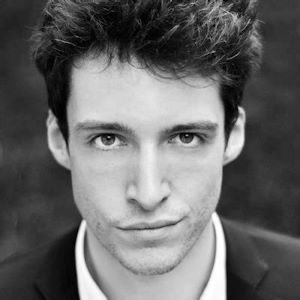 A man with short dark hair wearing a shirt and blazer.