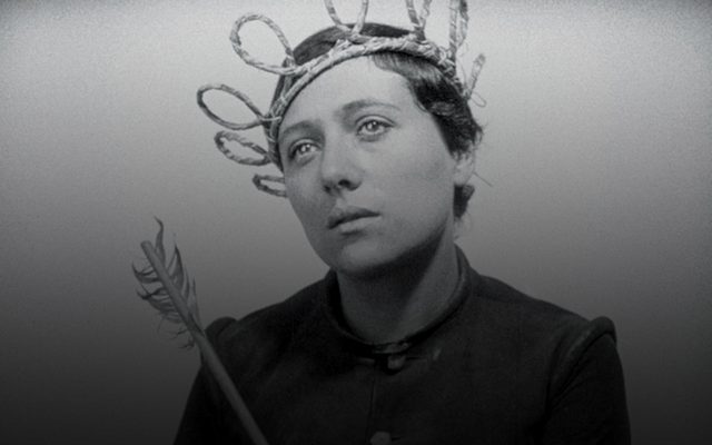 black and white still of a woman with close cropped hair wearing a woven reed crown and holding a quill