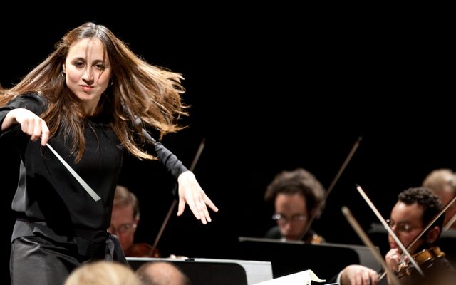 A lady with long hair conducts an orchestra