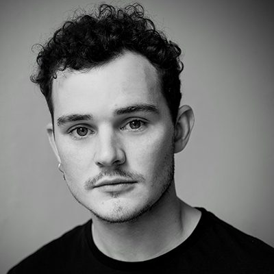 A man with short curly hair and a slight moustache.