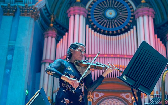 A woman playing the violin in front of a large organ.
