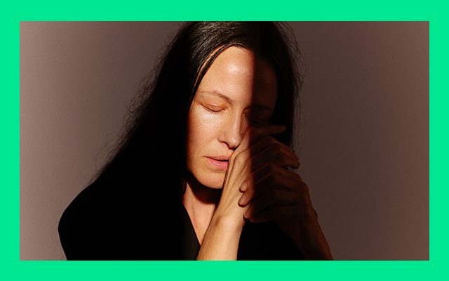 A woman with hands clasped, half in shadow