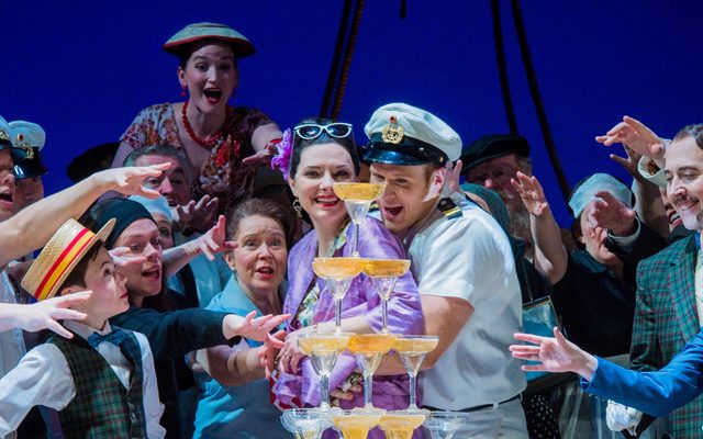 A group of people reaching for a pyramid of drinks. Among them are sailors.