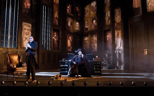Two men in old-fashioned dress in a grand hall decorated with portraits