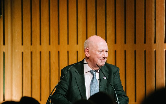 A man wearing a blue tie is stood at a lectern.