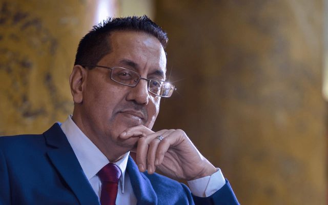 A man wearing glasses with his finger on his chin.