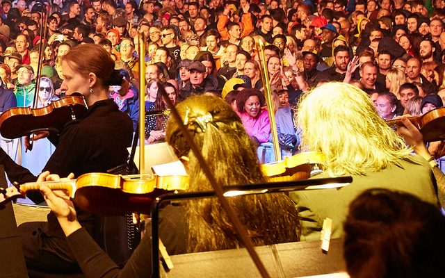 An orchestra playing in front of a large crowd.
