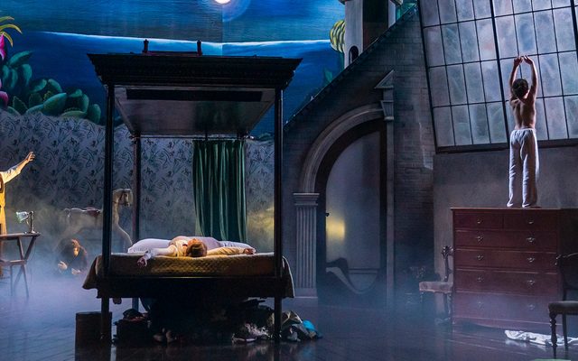 A ghostly scene with a central bed and boy looking out of the window in pyjama bottoms.