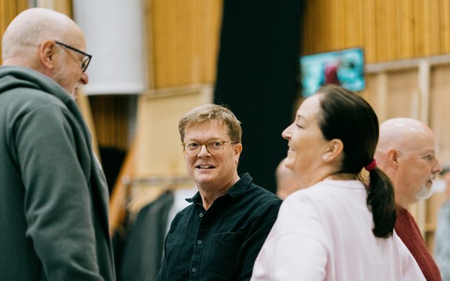 Two men and a woman are having a conversation, they are all smiling.