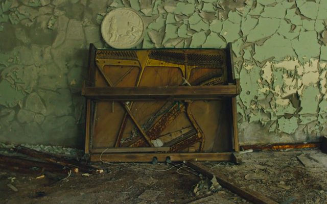 A ruined piano against a peeling light green wall, surrounded by debris