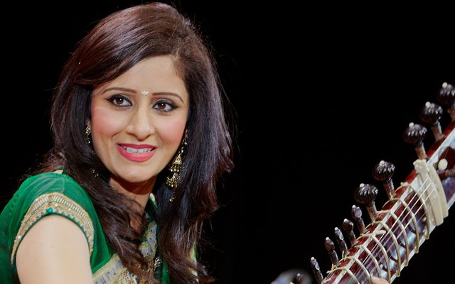 A woman in a green sari playing a sitar