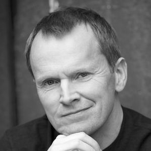A man with short hair resting his head on his hands.