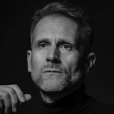 A black and white close-up picture of a man with a beard looking into the distance thoughtfully