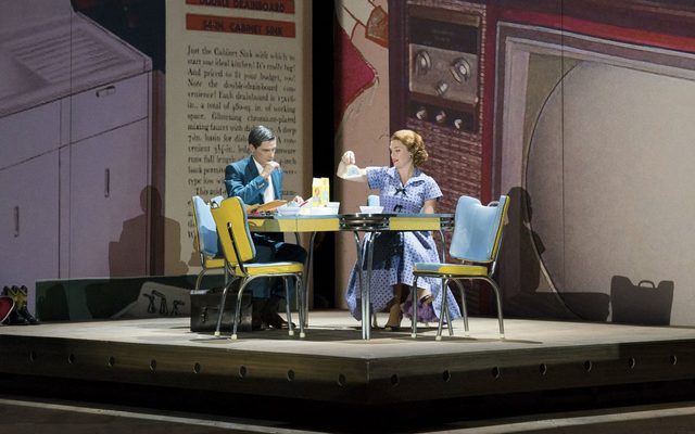 A man and women in 1950s costume sit at a table eating breakfast.