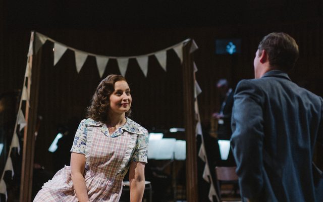 A girl sits under a string of bunting and looks lovingly towards a man who is approaching her