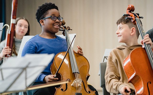 Two children smiling and holding cellos.