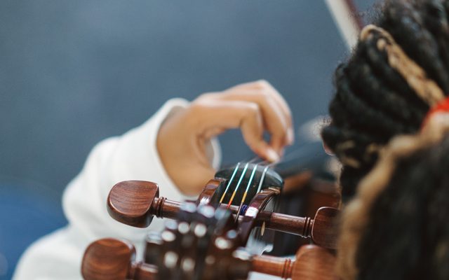 a close-up of the back of a young Black schoolgirl with braided hair playing a stringed instrument