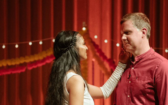 A woman in a dress touches the face of a man in a red shirt.