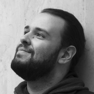 A man in a hoodie looking up while leaning against a wall.
