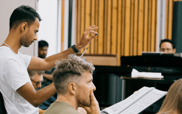 A man in a white t-shirt conducting musicians.