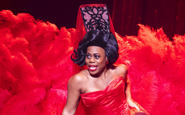Mezzo Chrystal E Williams as Carmen in Carmen. She is sat on the floor singing dressed in red and surrounded by red feathers.